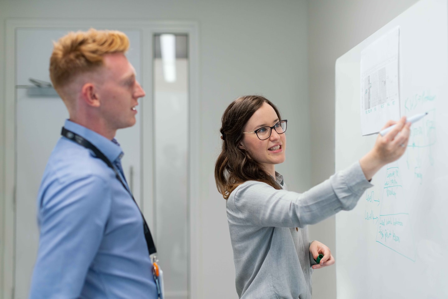 Due professionisti collaborano a una lavagna in un ufficio moderno.
