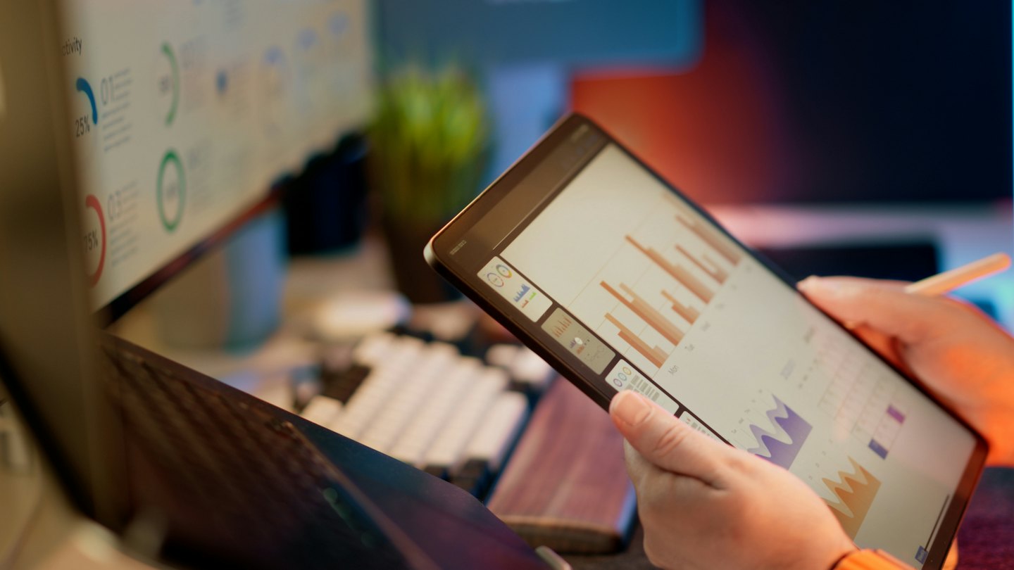 Persona che analizza grafici aziendali su un tablet alla scrivania.